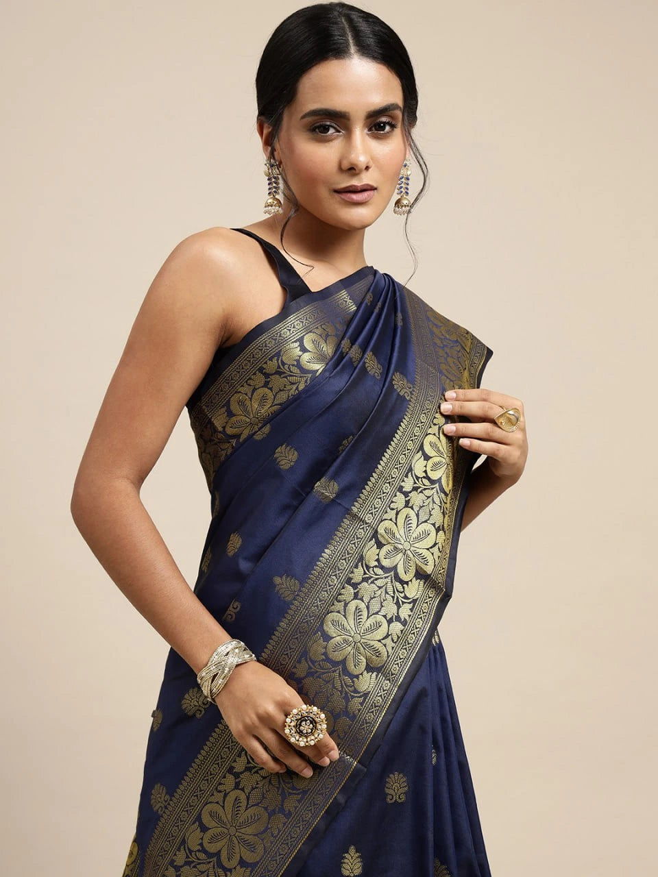 Woman wearing a navy blue saree with gold embroidery on a beige background